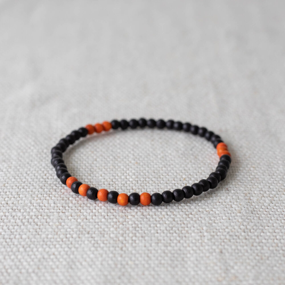 Minimalistisches Holzarmband mit schwarzen und orangen Perlen, inspiriert vom Kreuzfuchs – stilvoll, leicht und perfekt für den Alltag.