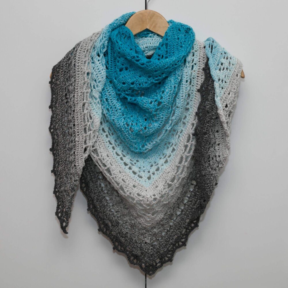Handgefertigtes Dreieckshäkel-Tuch aus Ombre-Garn in Blau- und Grautönen, stilvoll, vielseitig und komfortabel für den Alltag.
